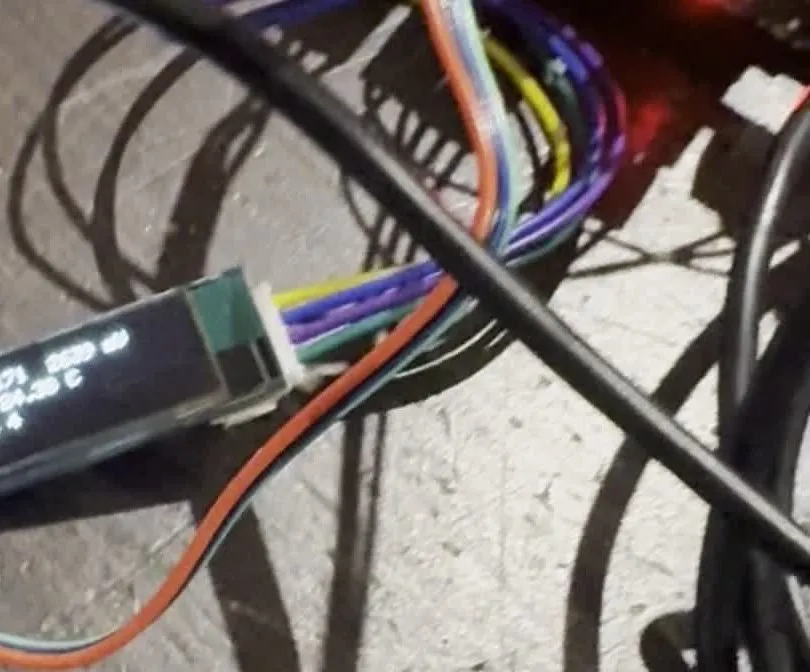Photograph of the small OLED display on the bench, lit with three lines of readings, among the harness wiring.